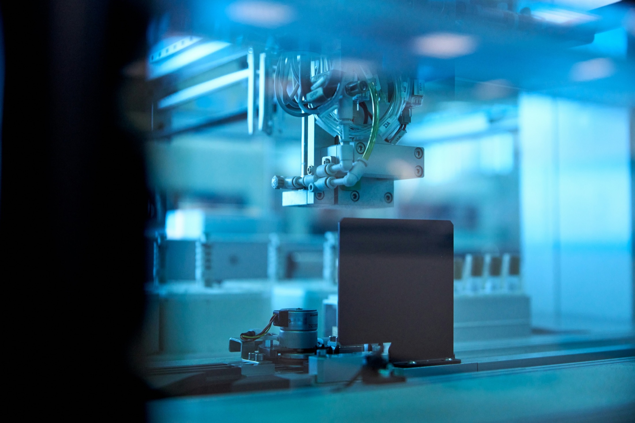 Precision robotic assembly head over a component plate in cool lab light